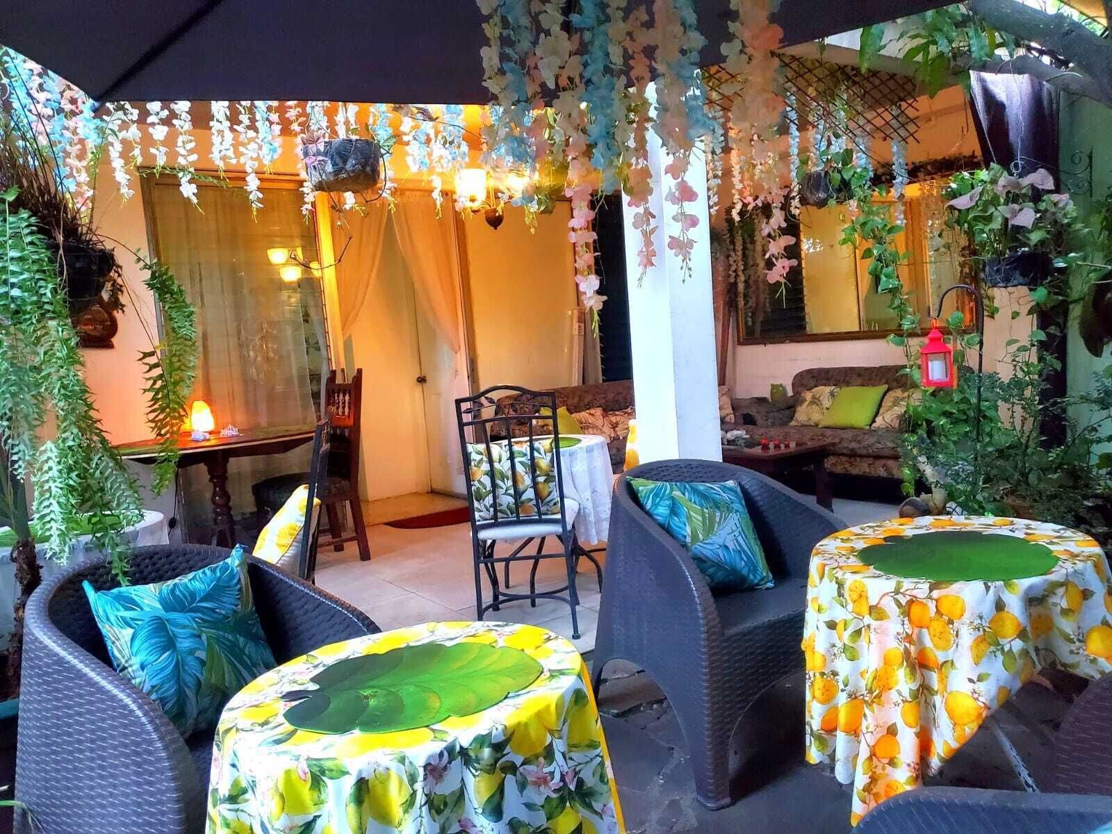 An outdoor seating area with wicker furniture, covered by a canopy, and decorated with hanging plants and lights.