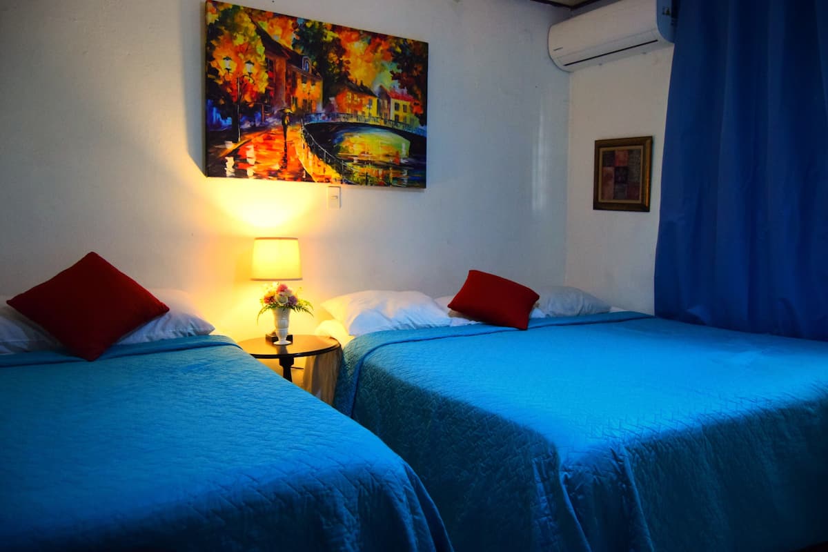 A hotel room with two beds, each with a red pillow, a nightstand with a lamp, and a painting on the wall.