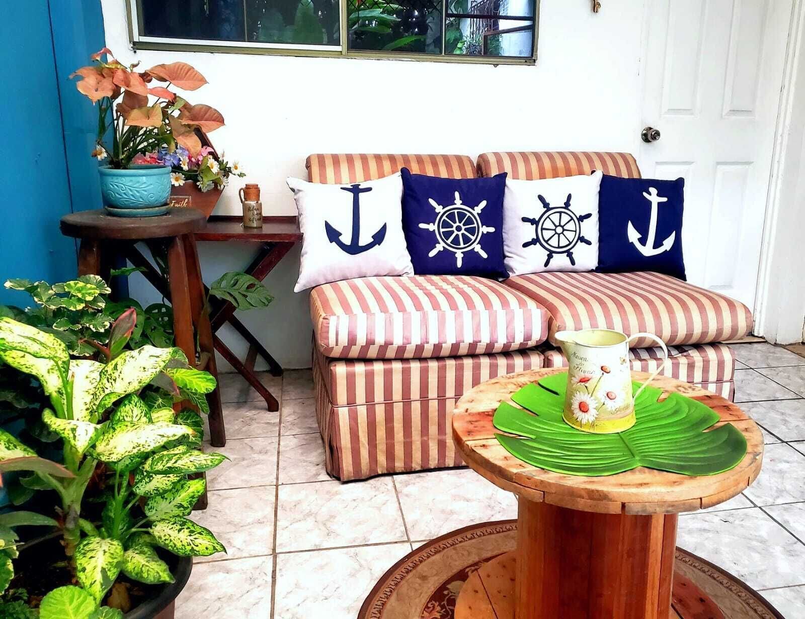 En hyggelig opholdsstue med en stribet sofa, maritime puder, et lille bord med en grøn måtte og krukkeplanter.