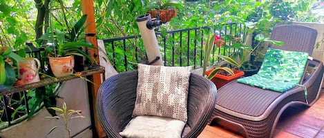 Una silla de mimbre con cojín, una tumbona con cojín y una mesita con un adorno.
