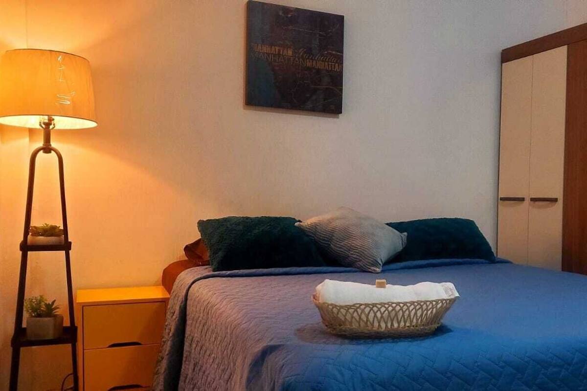 A bedroom with a bed, a nightstand, a lamp, a wall art piece, and a wardrobe.