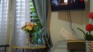 A room with a television mounted on the wall, a table with a vase of flowers, and a window with curtains. - Alojamiento El Salvador: Villa Madero - Hotel Boutique (San Salvador)