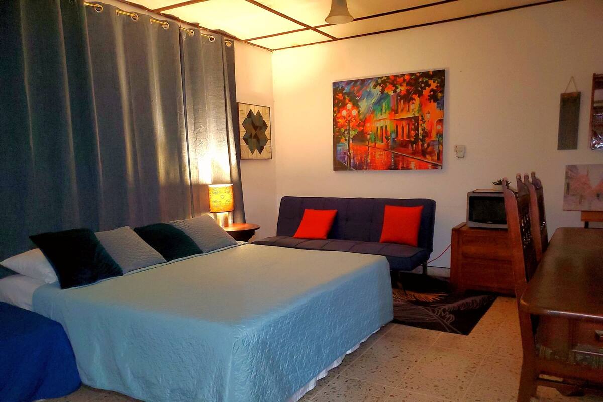 A bedroom with a bed, a sofa, a TV, and a painting on the wall.