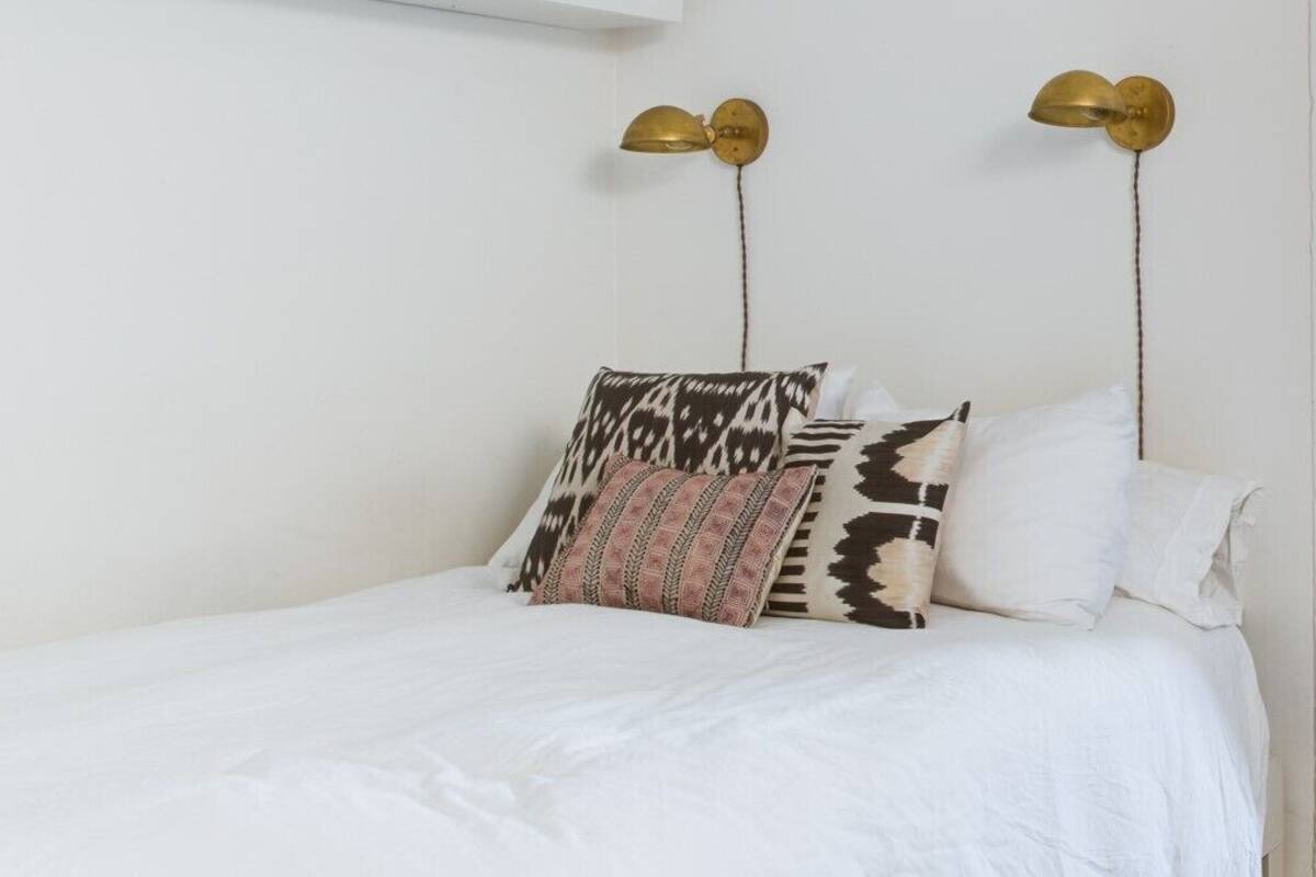 A bed with white bedding, two patterned pillows, and two wall-mounted lamps.