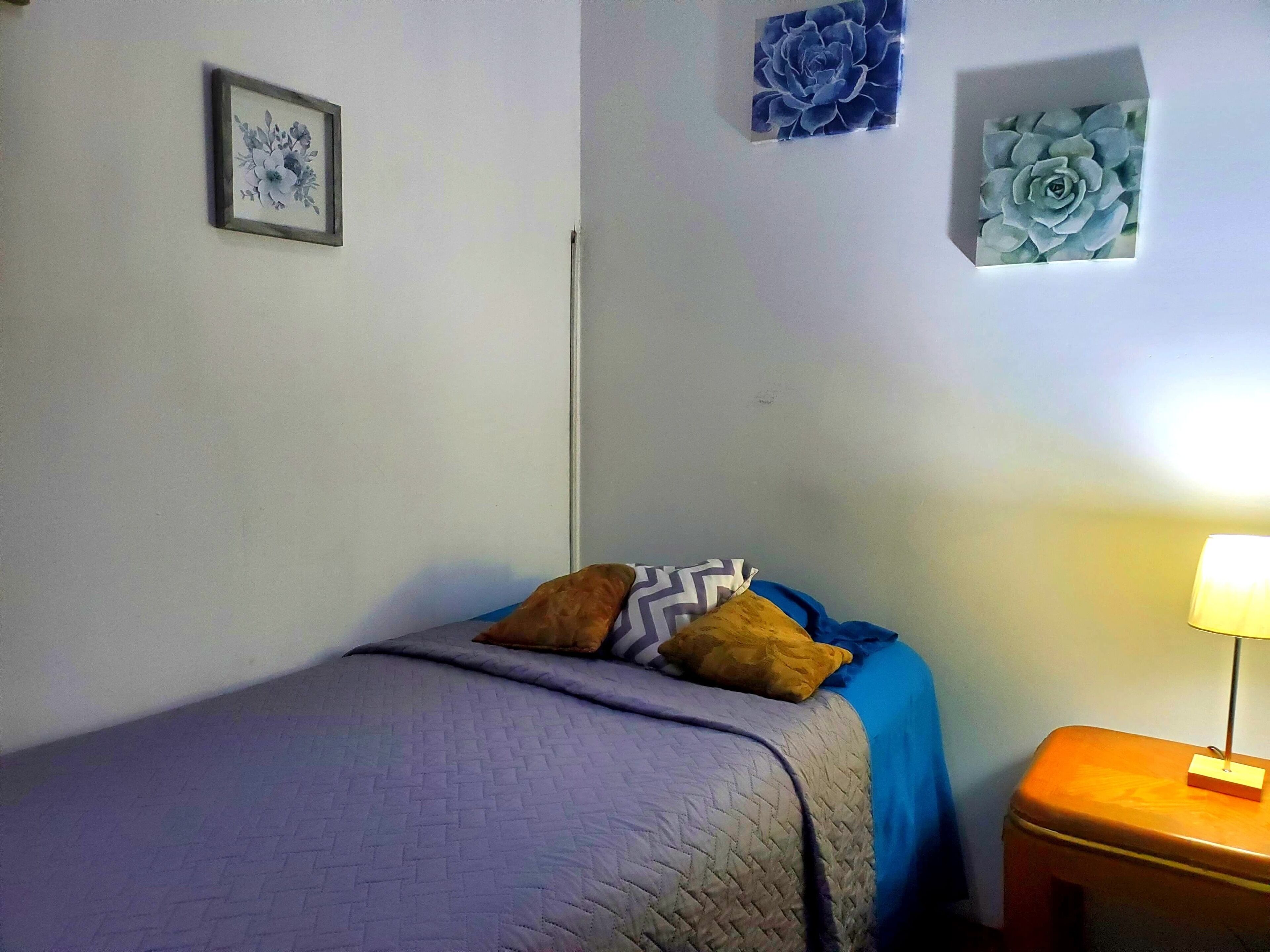 Une chambre à coucher avec un lit, une table de chevet, une lampe et des œuvres d’art murales.