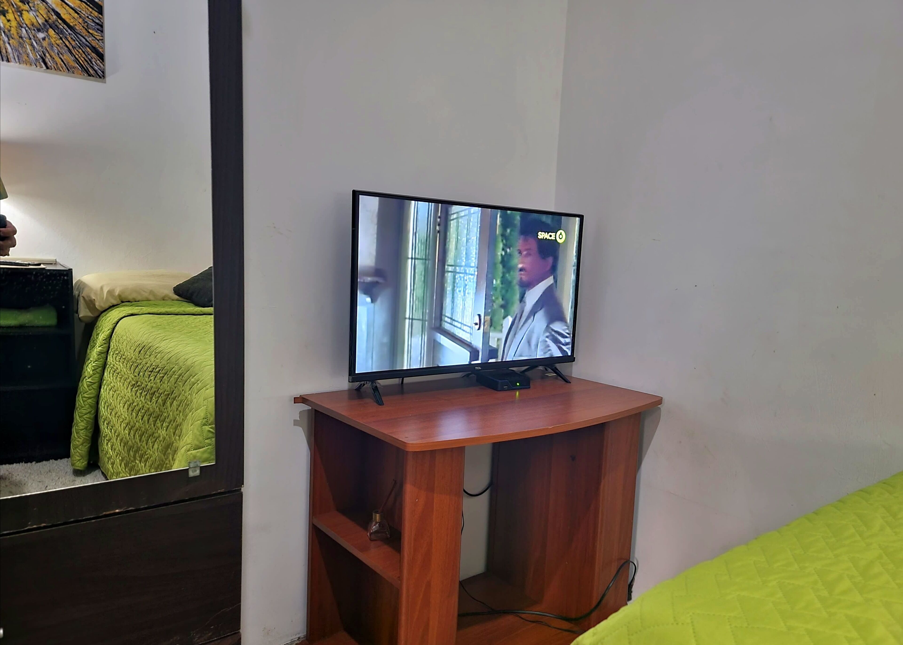 A television on a wooden stand in a room with a green bedspread and a white wall.