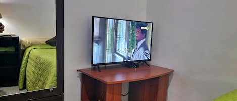 A television on a wooden stand in a room with a green bedspread and a white wall.