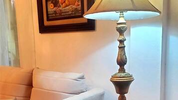 A room with a white armchair, a round black table with a lamp, and a framed artwork on the wall.