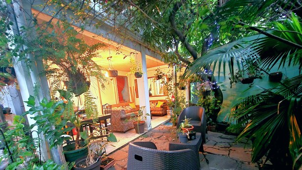 A cozy outdoor patio area with wicker furniture, potted plants, and a stone floor. - Alojamiento El Salvador: Villa Madero - Hotel Boutique (San Salvador)