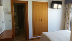 A room with a wooden wardrobe, a bed, a television, and a bathroom visible through an open door. - Hostal Mediterráneo (El Ejido)