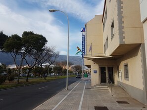 A street with a parking sign, a building with a Mediterranean flag, and a mountain in the background. - Hostal Mediterráneo (El Ejido)
