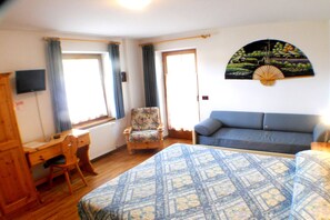 Una habitación con cama, escritorio, silla, sofá y ventilador de pared.
