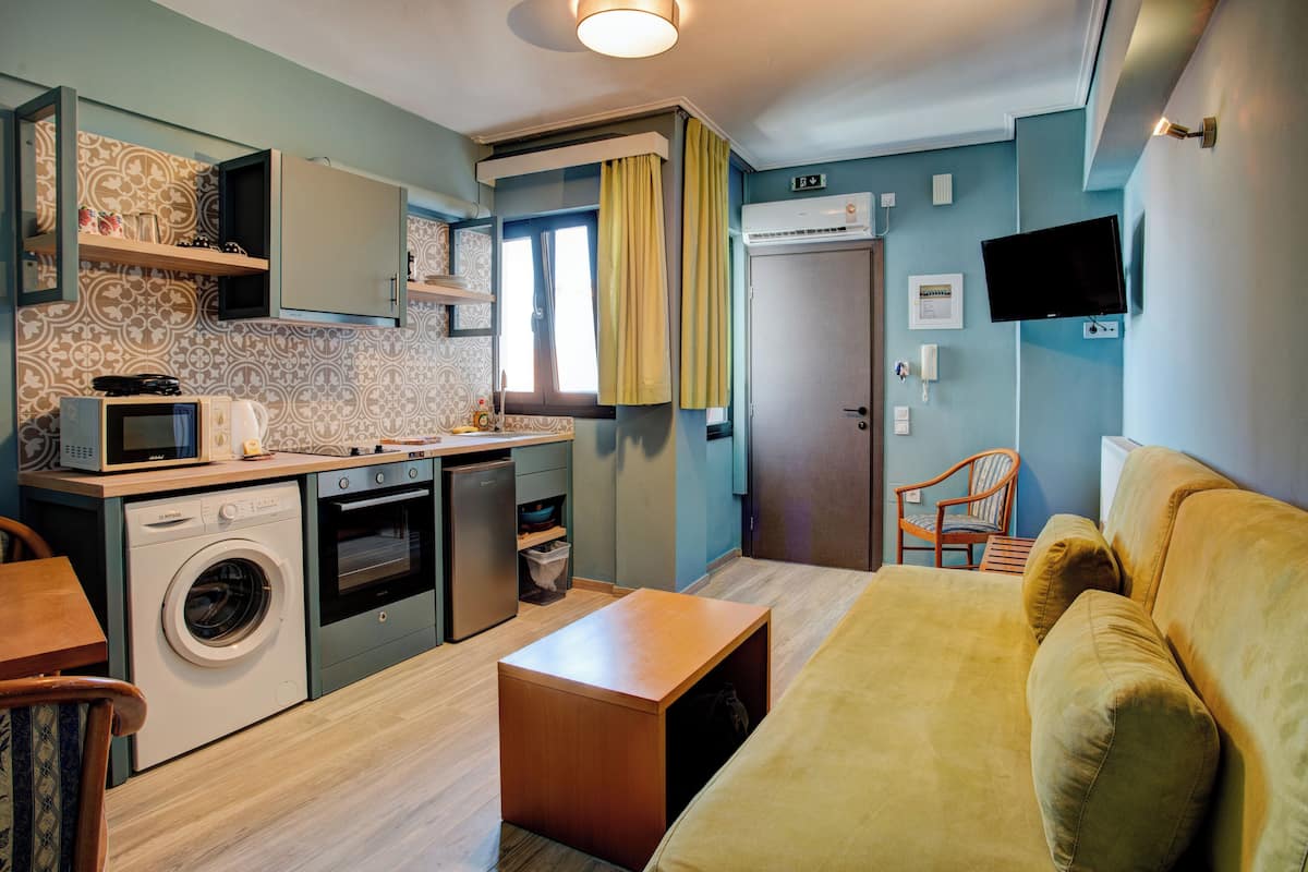 A compact kitchen with a washing machine, microwave, and oven. There is a sofa and a small table in the living area.