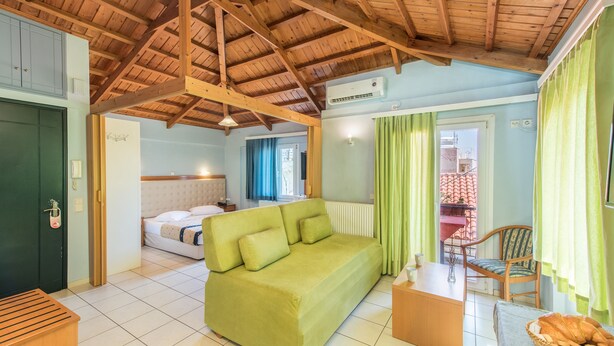 A room with a green sofa, a wooden bench, a chair, a small table, and a window with curtains. - Heliotrope The Studios (Lesvos)