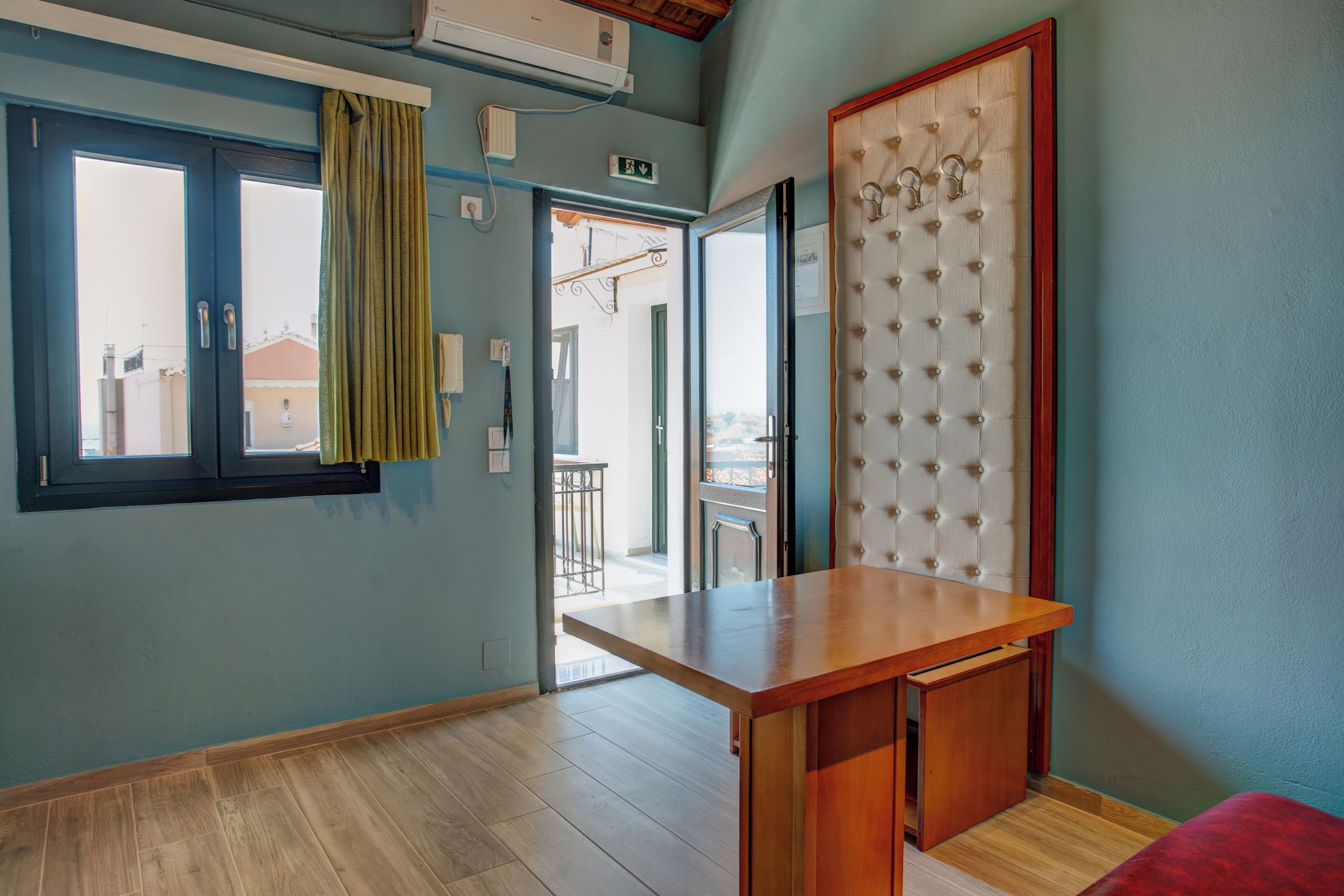 A room with a wooden desk, a window with a curtain, and a view of the outside.