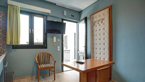 A room with a wooden desk, a chair, a tufted headboard, and a window with a curtain. - Heliotrope The Studios (Lesvos)