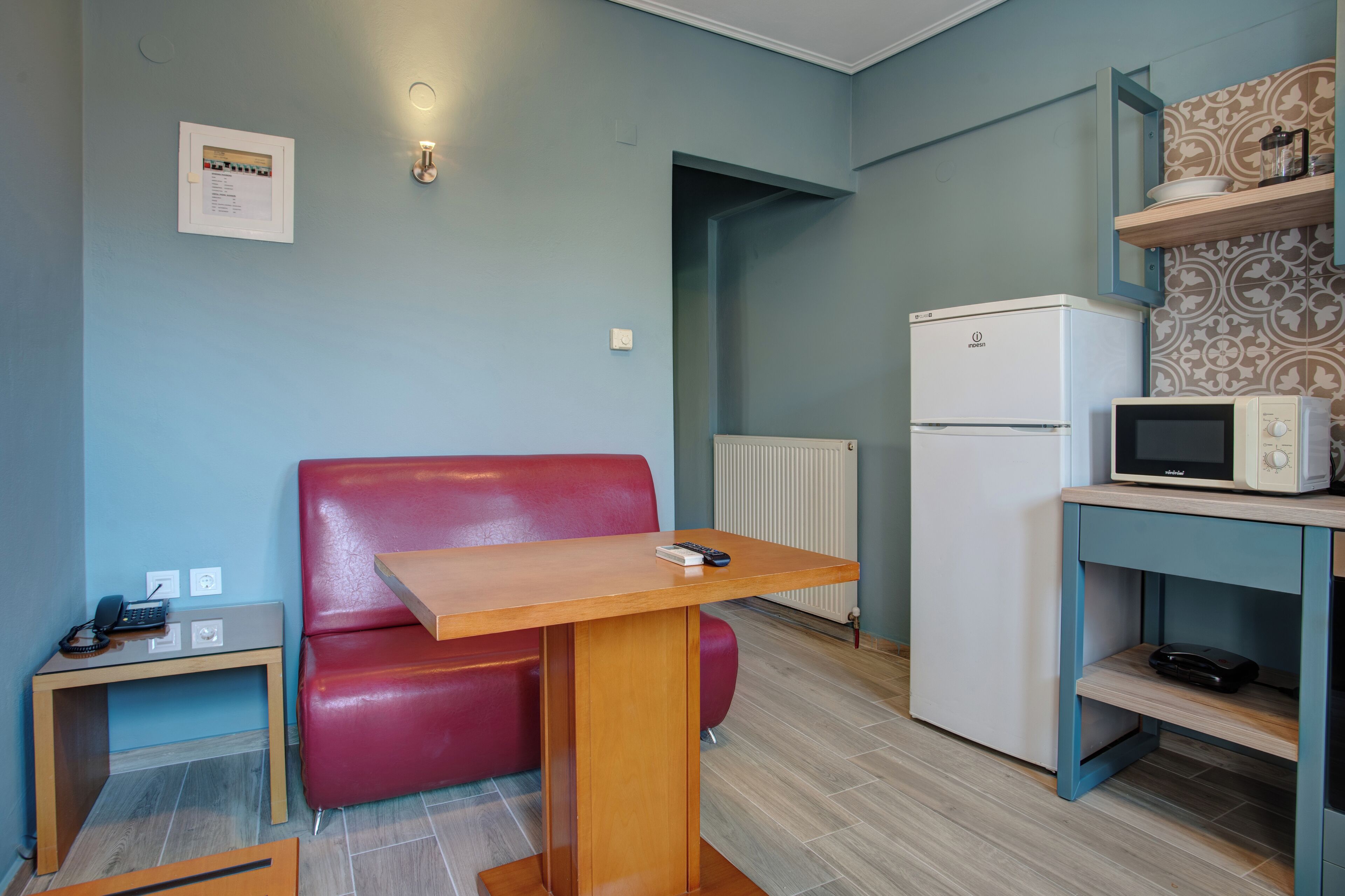 Una cocina compacta con un sofá de cuero rojo, una mesa de madera, un refrigerador blanco, un microondas y un mueble pequeño con papel tapiz estampado.