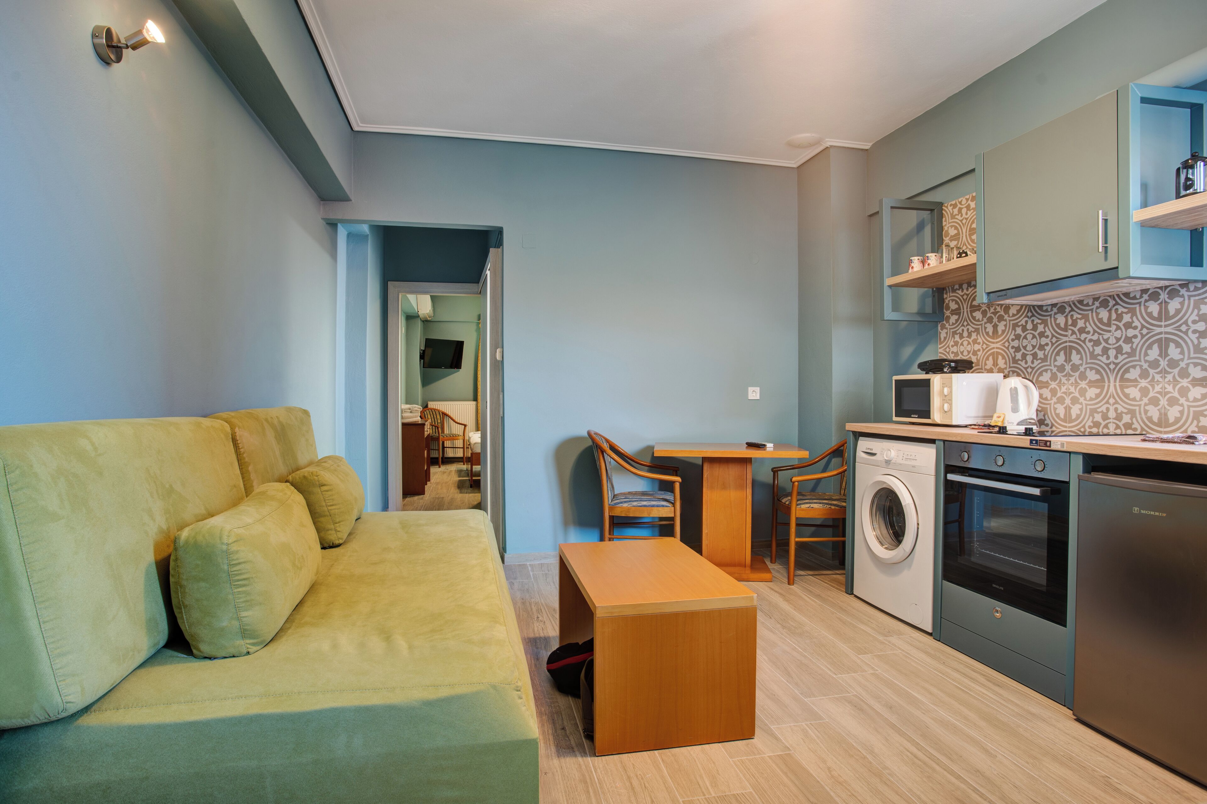 A compact living space with a sofa, a wooden bench, a washing machine, an oven, and a microwave.