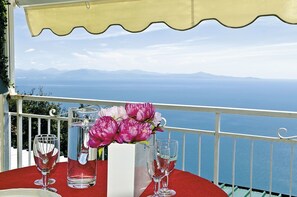 A table with a red tablecloth, a pitcher, and a vase with flowers, overlooking a scenic view of the sea and mountains. - Leonardo's B&B (Agerola)