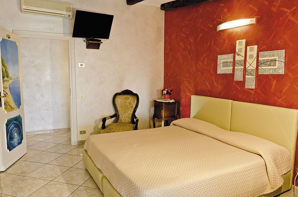 Un dormitorio con cama, una silla, una mesita y televisor de pared.