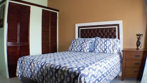 Un dormitorio con una cama grande, un armario de madera y una mesita de noche con un jarrón.