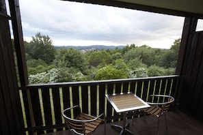 En balkon med et bord og to stole, der udover et frodigt landskab med træer og fjerne bakker.