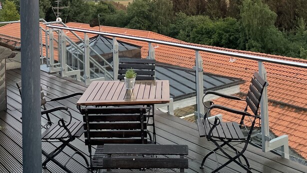 A balcony with a view of a rainbow, a tiled roof, and surrounding greenery. - Berghotel Sankt Andreasberg (Braunlage)