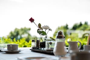 Et bord dækket med en hvid kop, underkop, en krystal kande, sukker skål og en lille vase med en rose og hvide blomster.