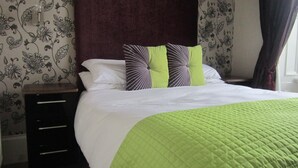 A neatly made bed with a green quilt, two pillows with a striped pattern, and a dark headboard. - The Royal Hotel (Girvan)