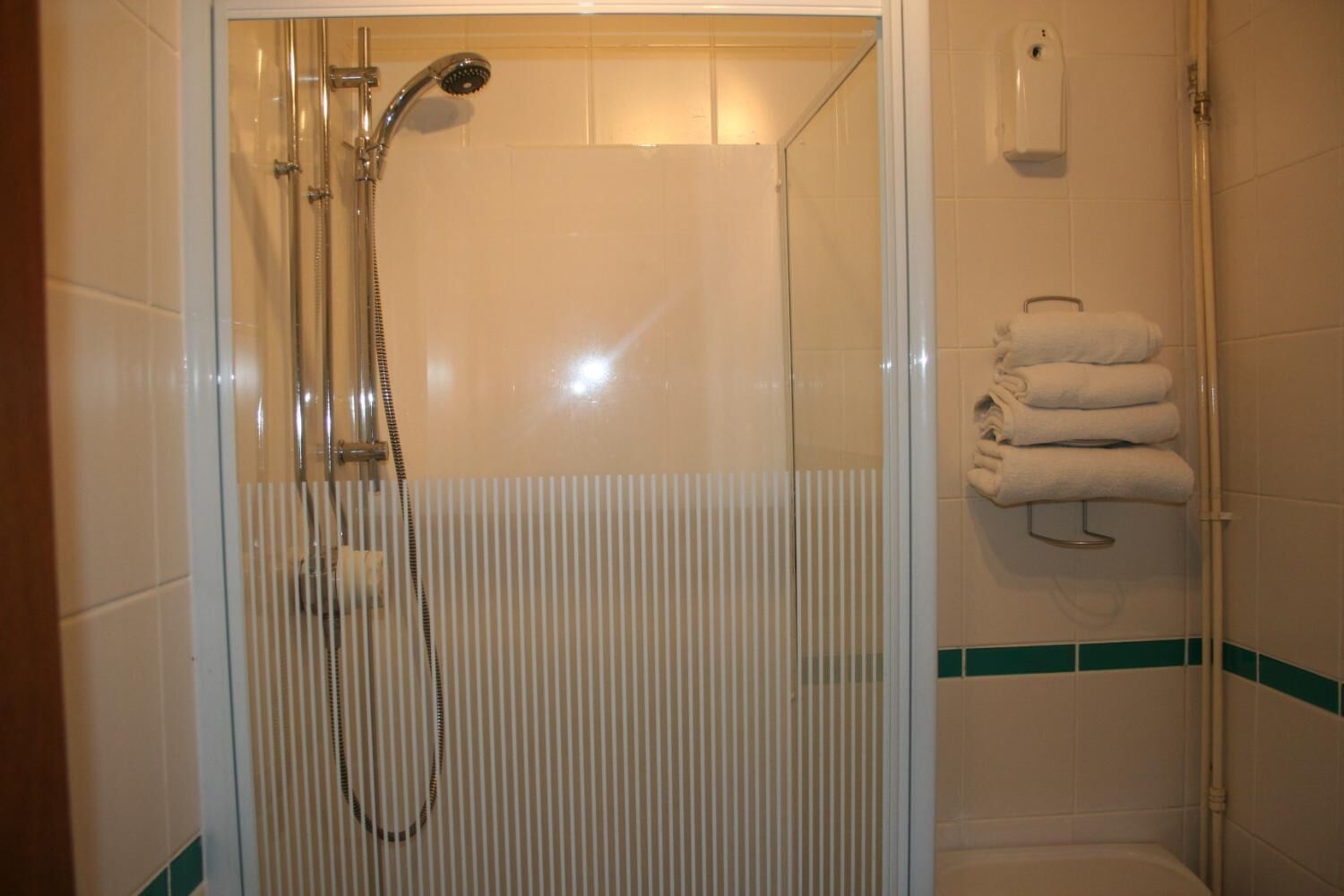 Une douche avec une porte en verre, un porte-serviettes avec des serviettes pliées et un sèche-mains fixé au mur.