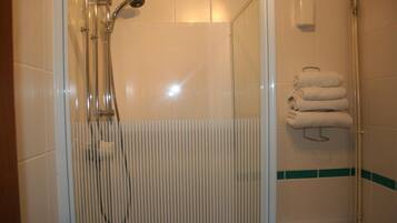 Une douche avec une porte en verre, un porte-serviettes avec des serviettes pliées et un sèche-mains fixé au mur.