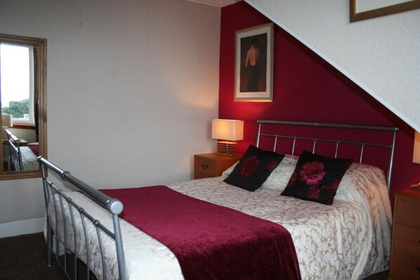 A bedroom with a bed, a nightstand, a lamp, a mirror, and a red wall.
