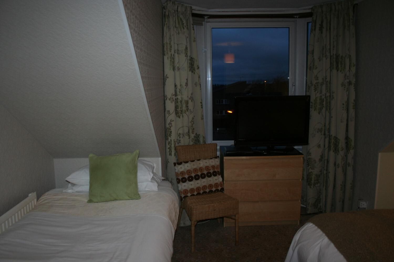 A hotel room with a bed, a television on a dresser, a chair, and a window with a view of the night sky.