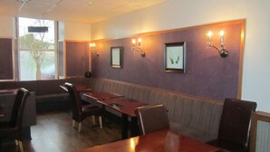 A restaurant with booths and tables, wall-mounted light fixtures, and framed pictures. - The Royal Hotel (Girvan)