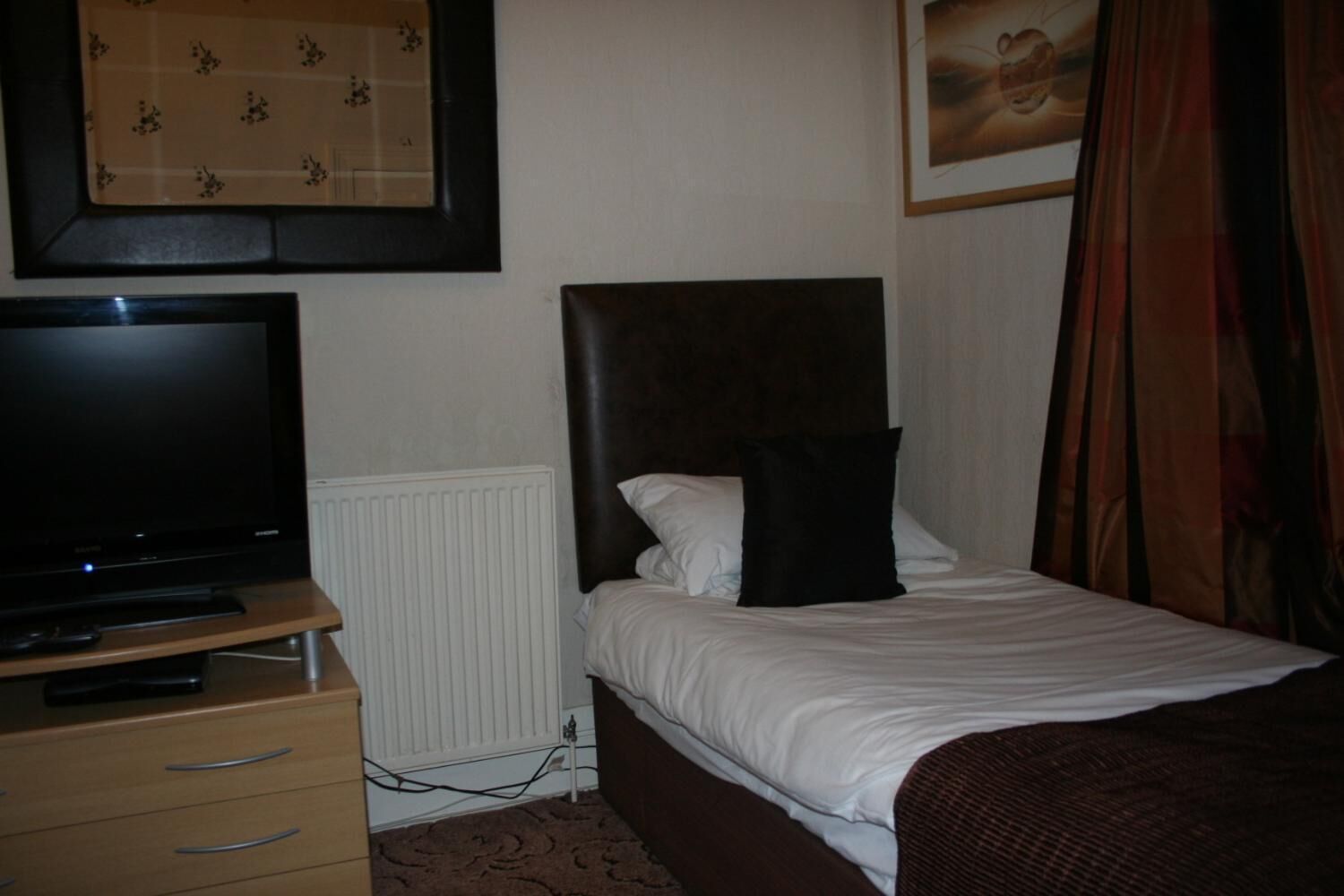 Ein Hotelzimmer mit Bett, Fernseher auf einem Holztisch, Heizkörper und einem gerahmten Bild an der Wand.