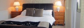 A neatly made bed with a black headboard, two bedside tables with lamps, and a wooden nightstand with drawers. - The Royal Hotel (Girvan)