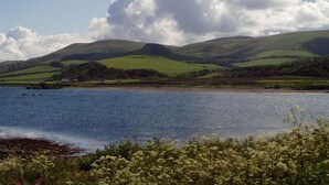 A coastal landscape with a body of water, green hills, and a clear sky. - The Royal Hotel (Girvan)