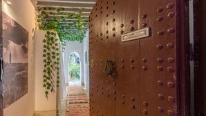 A hallway with a patterned carpet, a large wooden door with metal studs, and a hanging green vine. - Riad Tchaikana (Marrakech)