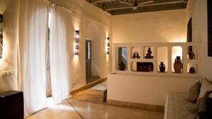A hotel room with a bed, a sofa, a wall-mounted shelf with decorative items, a ceiling fan, and a window with curtains. - Riad Tchaikana (Marrakech)