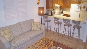 Um espaço compacto com cozinha compacta, sofá listrado, mesa de centro e área com banquetas.