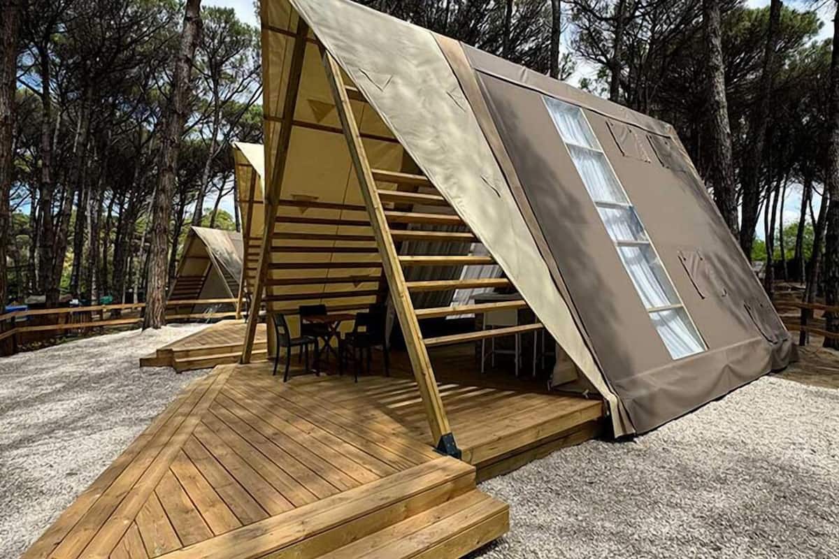 A modern, triangular tent-like structure with a wooden deck and a staircase leading to an upper level.
