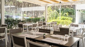 Un restaurante al aire libre con mesas, sillas, ventanas amplias y vistas a zonas verdes.