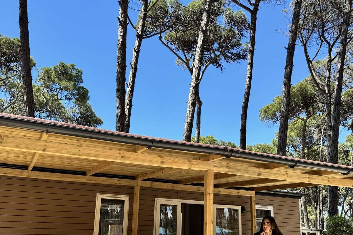 A wooden cabin with a balcony, large windows, and a view of tall trees.