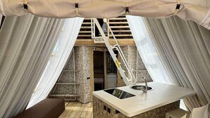 Una carpa con una terraza de madera, una pequeña zona de bar y una escalera que conduce a un nivel superior.