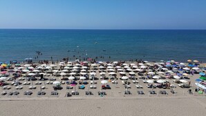 Una playa con numerosos paraguas y tumbonas, lo que sugiere un ambiente de complejo turístico.