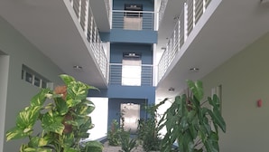 A multi-level atrium with a central elevator, surrounded by potted plants and pebbles. - New Kingston Luxury Apt The Bromptons (Kingston)