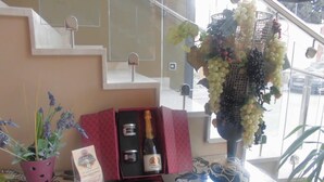 Un espace d’accueil d’hôtel avec une table en verre sur laquelle sont disposés une bouteille de champagne, un vase de raisins et une plante en pot.