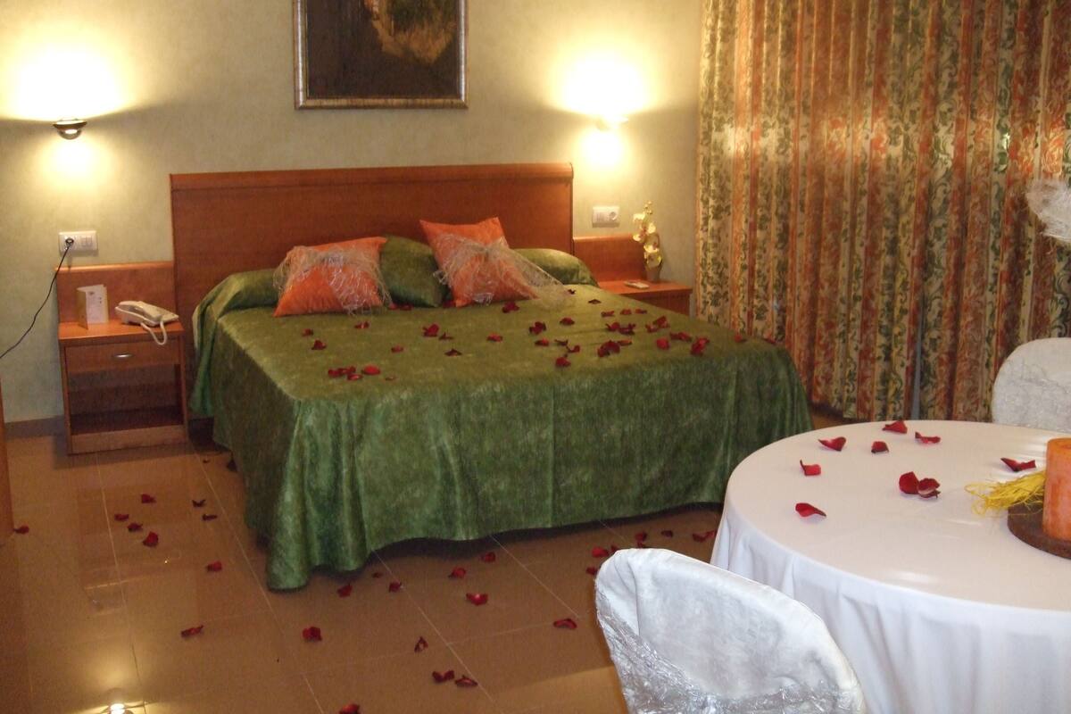 A hotel room with a bed, two bedside tables, a nightstand, a painting on the wall, and a curtain.