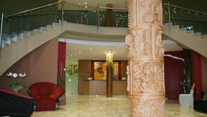 Un hall d’entrée doté d’un sol en marbre, d’un comptoir de réception, d’un escalier et d’une grande colonne décorative.