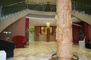 Un vestíbulo con piso de mármol, una mesa de recepción, una escalera y una gran columna decorativa.